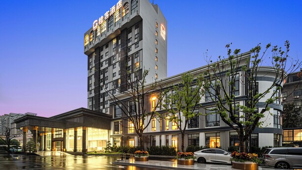 Un hôtel à plusieurs étages, doté d’un design moderne, avec une entrée imposante, de grandes fenêtres et une façade bien éclairée.