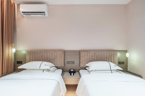 A hotel room with two beds, a nightstand, a wall-mounted air conditioner, and bedside lamps.