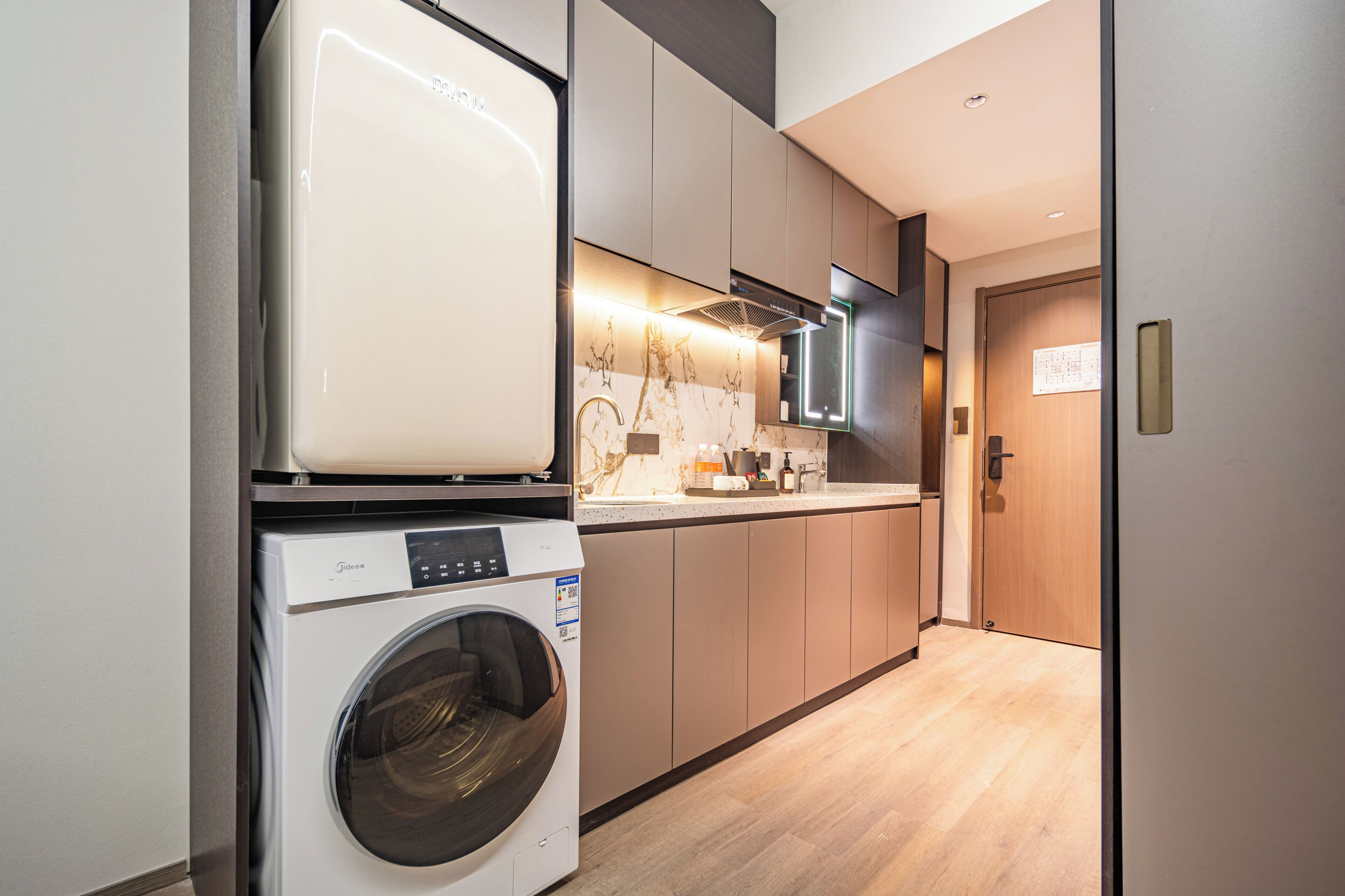 Een compacte keuken met een ingebouwde wasmachine en droger, houten kastjes en een marmeren spatwand.