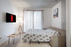 A bedroom with a bed, a desk, a lamp, a TV, and a painting on the wall. - Cozy hidden gem in the heart of Montreal (Montréal)