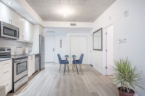A modern kitchen with stainless steel appliances, a dining area with blue chairs, and a potted plant. - Cozy hidden gem in the heart of Montreal (Montréal)