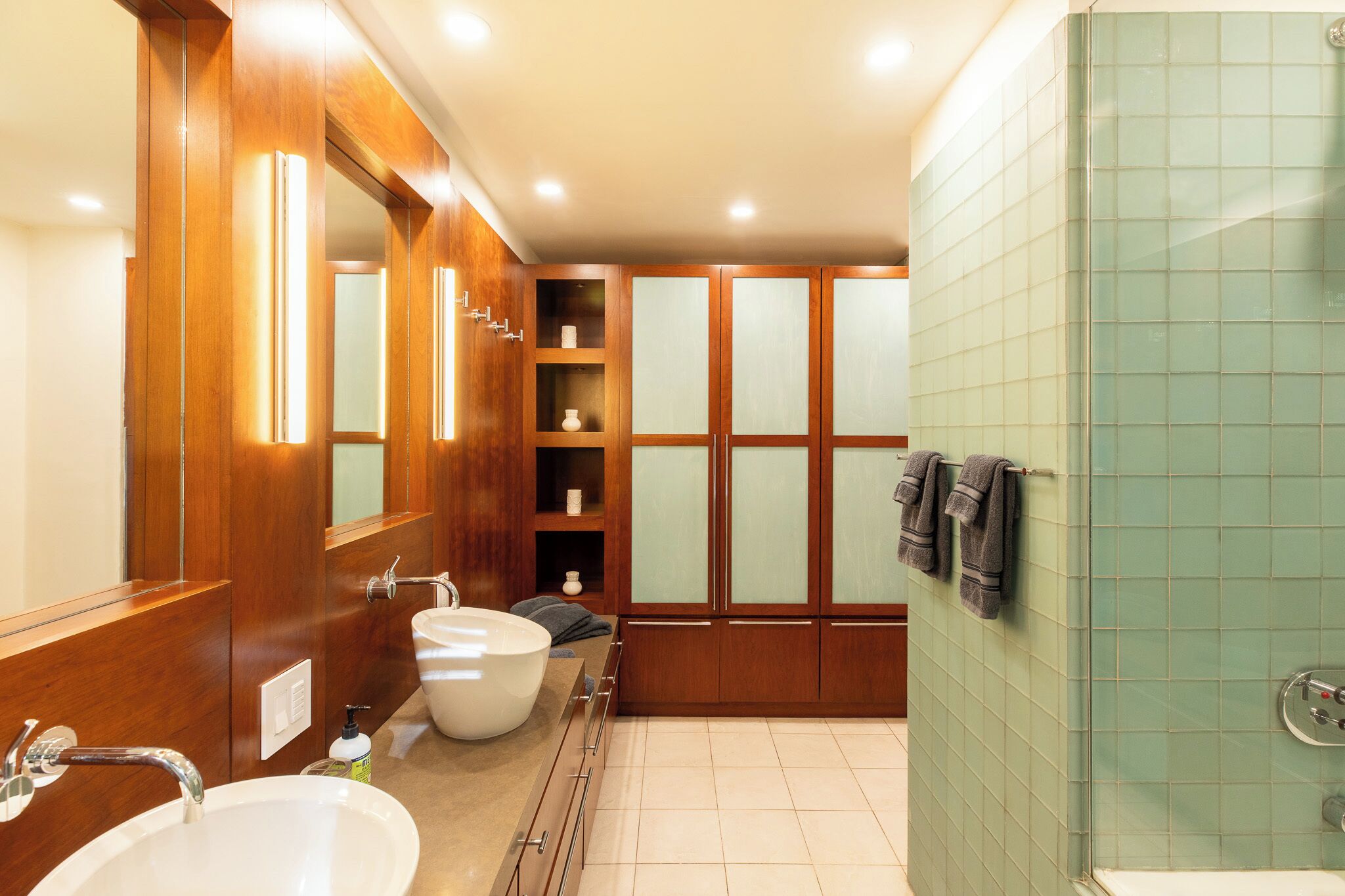 Une salle de bain avec deux lavabos, un grand miroir, des meubles en bois et une cabine de douche en verre.