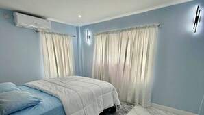 Une chambre à coucher avec un lit, des rideaux, un appareil de climatisation et un sol en marbre.
