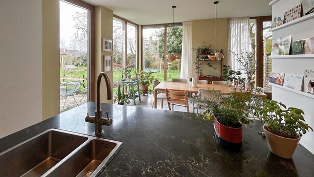 A kitchen with a double sink, dining area with a table and chairs, and a view of the garden through large windows. - 3 bedroom beautiful home in Steenenkamer (Steenenkamer)