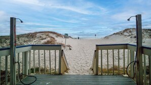 Un sentier en bois mène à une plage de sable, avec des dunes en arrière-plan.