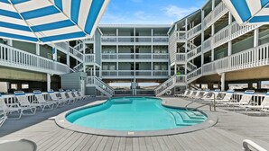 Un espace piscine doté de plusieurs niveaux de balcons, de chaises longues et d’une piscine centrale.