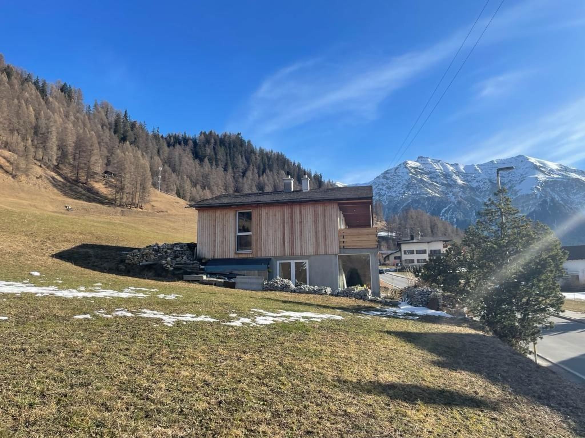 Un bâtiment moderne à deux étages, doté d’une façade en bois, situé dans une région montagneuse, avec des sommets enneigés en arrière-plan.