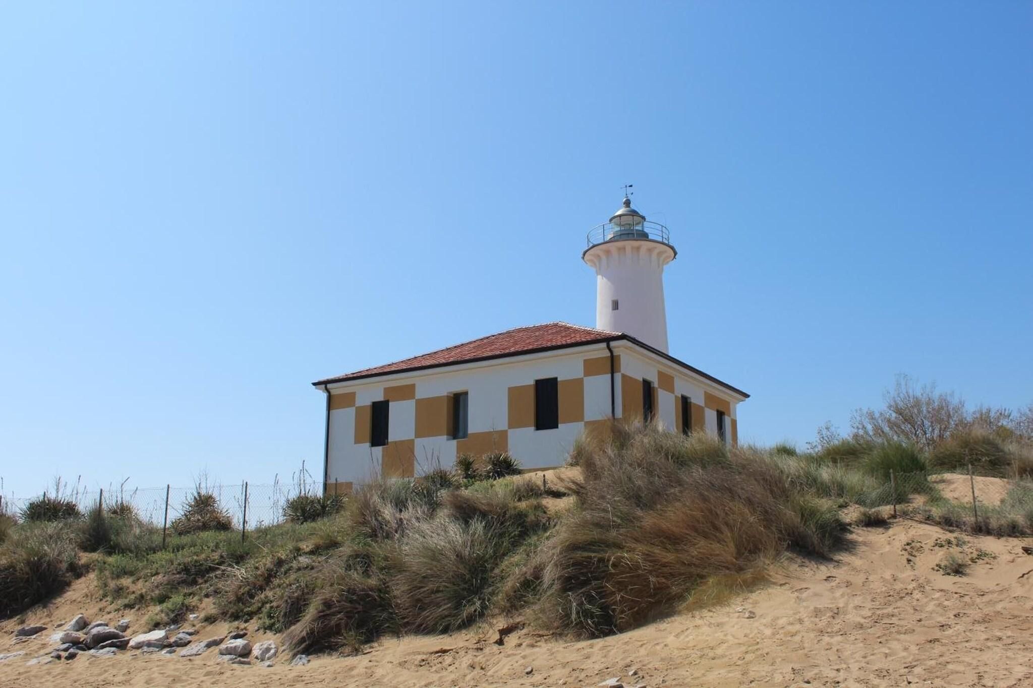 A lighthouse with a white exterior and a red roof, situated on a sandy hill with sparse vegetation.