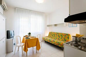 Un espace de vie compact comprenant un coin cuisine, un espace repas avec une table et des chaises, un canapé et un téléviseur.