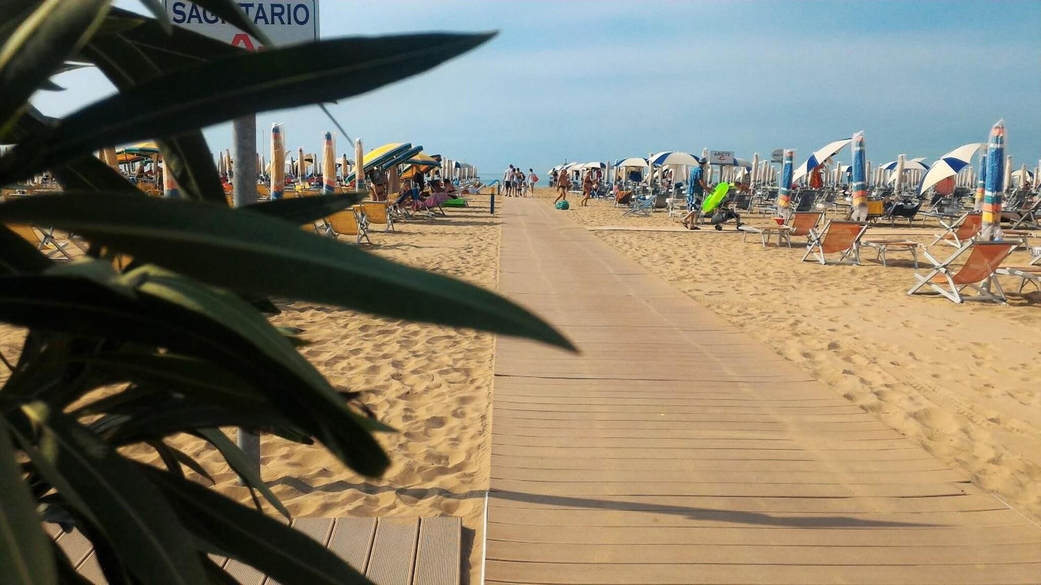 Una playa con un paseo de madera, sombrillas y sillas de descanso.
