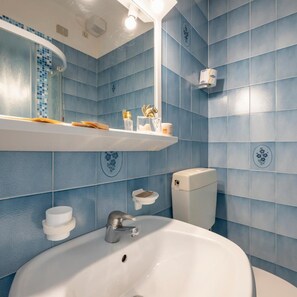 Ein Badezimmer mit einem weißen Waschbecken, einem Spiegel darüber und blautonierten Fliesen.