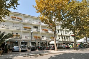 Un hotel a più piani con balconi, un’area di parcheggio e un negozio.