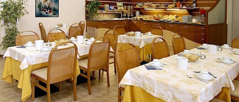 A dining area with tables set for breakfast, chairs, a buffet counter, and a wall-mounted picture.