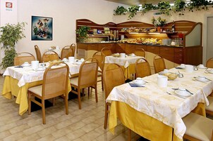 Zona pranzo con tavoli apparecchiati per la colazione, sedie, un banco buffet e un quadro appeso al muro.