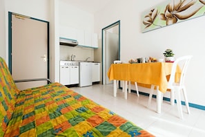 Une pièce comprenant un lit, une table à manger avec des chaises, un coin cuisine et une porte.