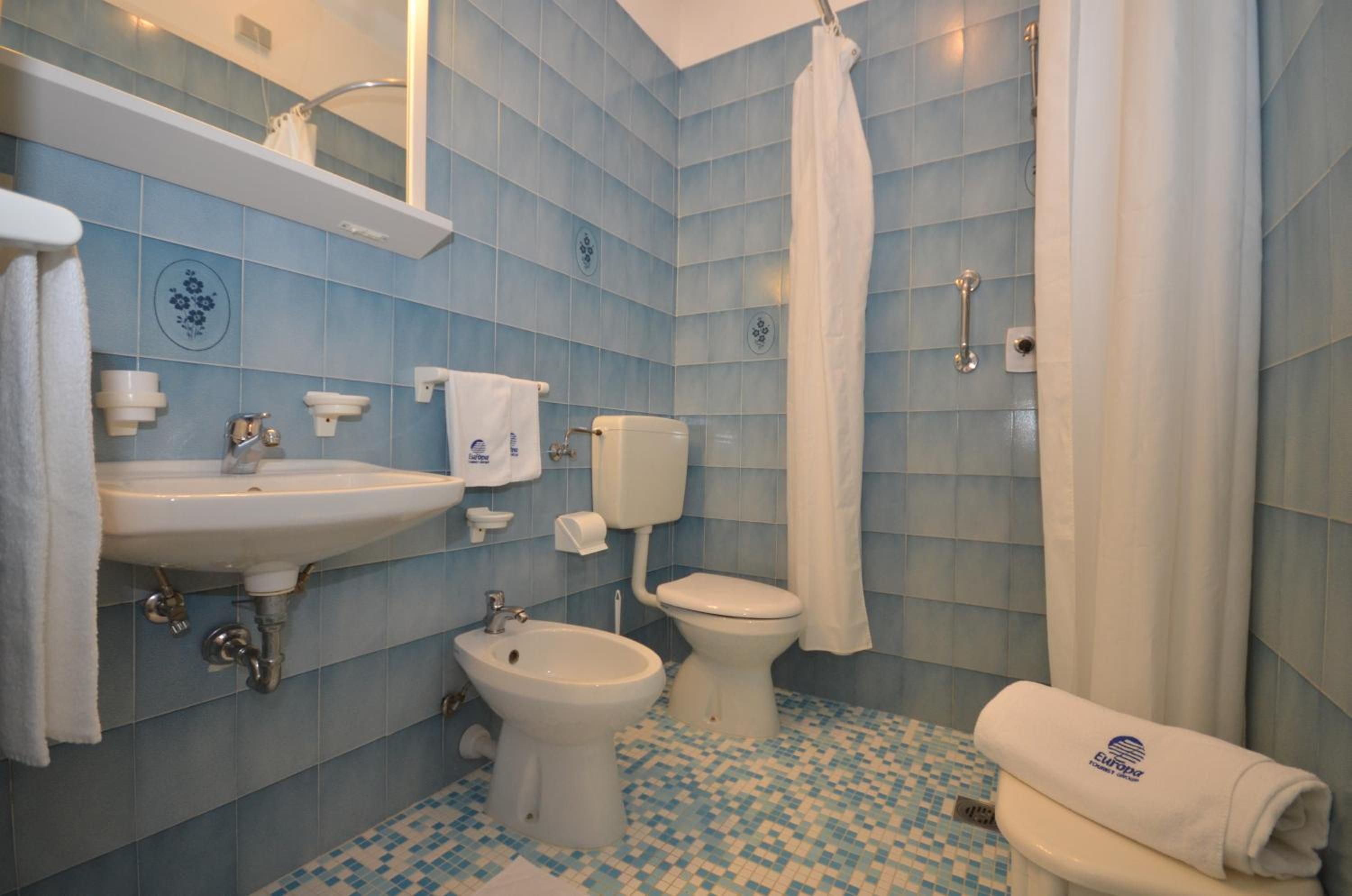 A bathroom with a sink, bidet, toilet, and shower curtain.