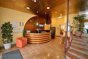 Un espace d’accueil comprenant un comptoir en bois, des plantes en pot, un escalier et un panneau indiquant clairement la sortie.