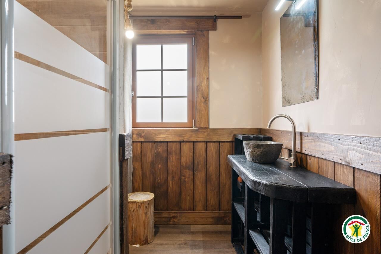 A rustic bathroom with wooden walls, a window, a sink, and a mirror.