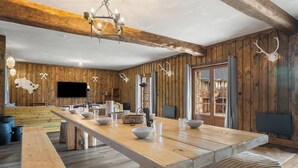 Ein rustikales Interieur mit einem großen Holzesstisch, einer Kandelaber und Geweihen an der Wand.