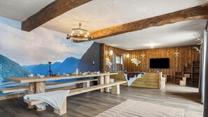 Ein rustikales Interieur mit Holzbalken, einem großen Holztisch, einem Kamin und einem Fernseher.