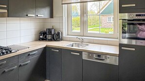 Een moderne keuken met donkere kastjes, een ingebouwde vaatwasser, een koffiezetapparaat en een raam met uitzicht op een huis.