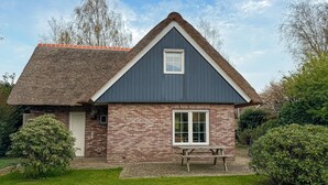 Een gelijkvloers huis met een puntig dak, een bakstenen gevel en een klein voortuintje met een bankje.