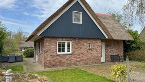 Een huis met een donkerblauwe gevel, een bakstenen onderstuk, een witte deur en een klein raam.