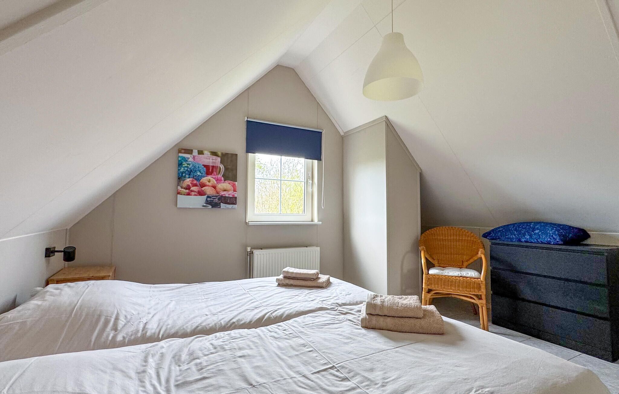 Ein Schlafzimmer mit zwei Betten, einem Fenster mit Blick, einem Heizkörper, einem Korbstuhl und einem Schminktisch.