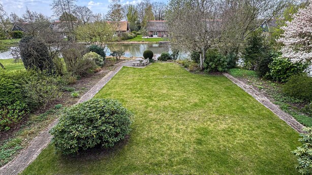 Een verzorgde tuin met een vijver, netjes gemaaid gras en verschillende struiken.