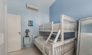 A bunk bed room with a door, a small bedside table with a lamp, and a painting on the wall. - Serenity by the Sea Duplex Bougainville Resort (Sarandë)