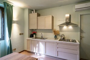 Een kleine keuken met een gasfornuis, spoelbak, kastjes en een raam met gordijnen.