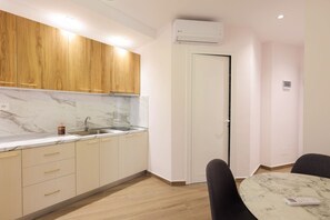 A modern kitchen with wooden cabinets, a marble countertop, and a dining area with a table and chairs. - Cozy Apartment 01 in Durr s (Durrës)