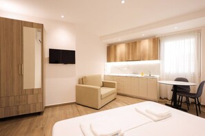 A hotel room with a bed, a chair, a desk, a TV, and a kitchenette. - Cozy Apartment 06 in Durr s (Durrës)