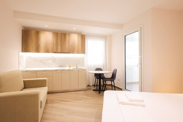 A modern hotel room with a bed, a small kitchenette, a dining area, and a balcony. - Cozy Apartment 06 in Durr s (Durrës)