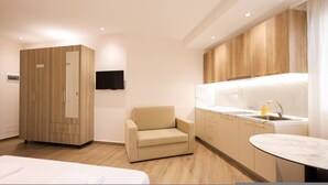 Een hotelkamer met een bed, een bank, een televisie, een kitchenette en houten kasten.