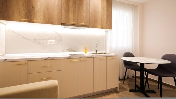 Een moderne keuken met houten kastjes, een marmeren aanrecht, een spoelbak en een eethoek met een ronde tafel en stoelen.