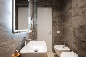 Uma casa de banho moderna com um espelho grande, secador de cabelo, lavatório e bidé.