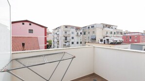 A balcony with a metal drying rack, a tiled roof, and multi-story buildings in the background. - Cozy Apartment 03 in Durr s (Durrës)