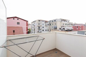 A balcony with a metal drying rack, a tiled roof, and multi-story buildings in the background. - Cozy Apartment 03 in Durr s (Durrës)