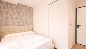 A bedroom with a bed, a marble-patterned wall, an air conditioning unit, and a door. - Cozy Apartment 03 in Durr s (Durrës)