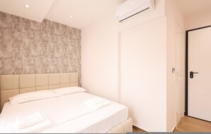 A bedroom with a bed, a marble-patterned wall, an air conditioning unit, and a door. - Cozy Apartment 03 in Durr s (Durrës)