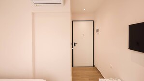 A hotel room with a white door, a mounted TV, and a ceiling air conditioner. - Cozy Apartment 03 in Durr s (Durrës)