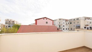 Terraço no telhado com telhas vermelhas, rodeado por edifícios com varandas e céu azul.
