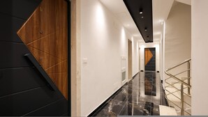 Um corredor moderno com porta de madeira, paredes brancas e chão de mármore que leva a uma escadaria.