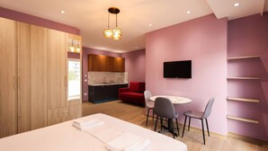 Quarto de hotel moderno com cama, escrivaninha, cadeira, televisão, sofá vermelho e área de cozinha.