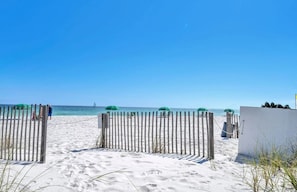 Ein Strand mit einer Holzbank, einem weißen Gebäude und grünen Sonnenschirmen.