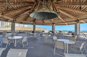 An outdoor patio with tables and chairs, a wooden ceiling, and a view of the ocean. - Jetty East 118B Gulf Views, Free Beach Service (Destin)