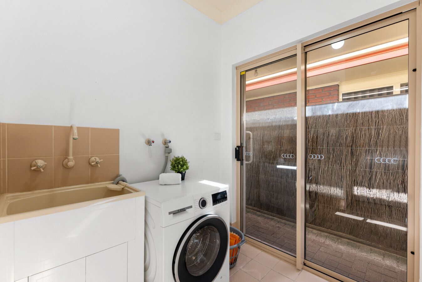 A compact bathroom with a washing machine, a bathtub, and a sliding glass door leading to a covered outdoor area.
