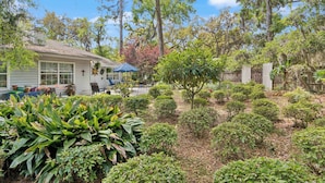 A house with a patio, surrounded by various plants and trees. - Pet Friendly Retreat | 3BR w/ Sunroom, Spacious Kitchen + Close to Beach (Saint Simons Island)