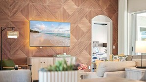 A modern living room with a geometric wooden wall, a flat-screen TV, a sofa, a coffee table, and a lamp. - Infinity Escape - 3BR with Boat Dock and Southern Exposure (Cape Coral)